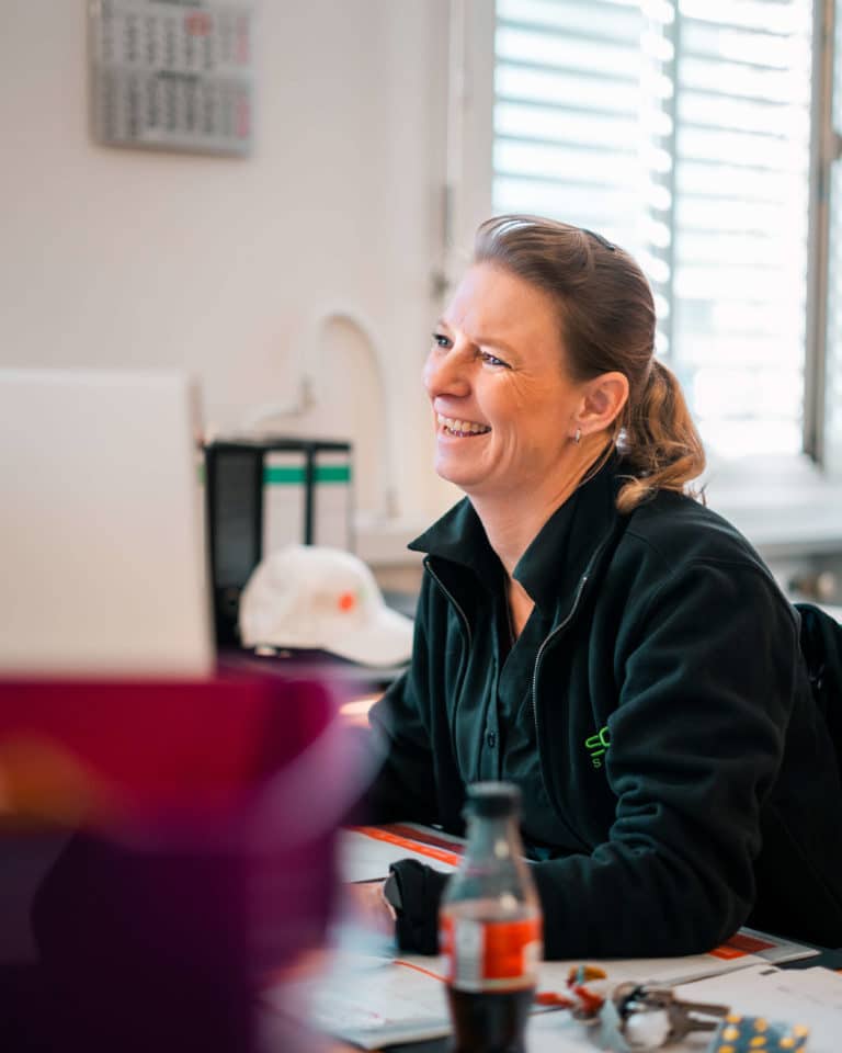 Freundliche und lächelnde Mitarbeiterin von Sitron am Schreibtisch.
