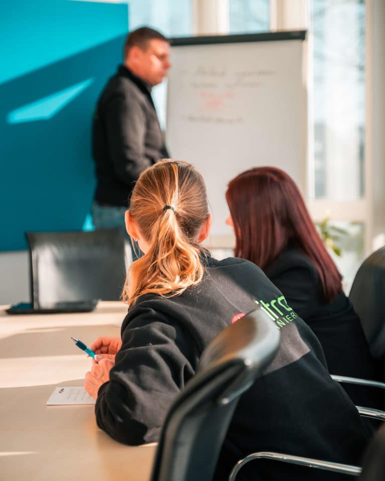 Zwei Mitarbeiterinnen in Arbeitskleidung am Besprechungstisch. Ein Projektleiter von Sitron erklärt die Aufgabenstellung am Flippchart.