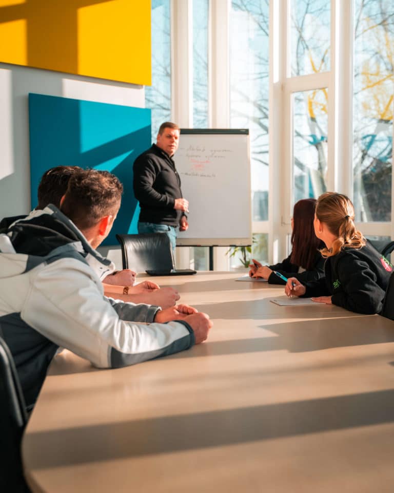 Vorarbeiter von Sitron steht am Flippchart und erklärt im Besprechungsraum mehreren Mitarbeitern Details über einen Auftrag.