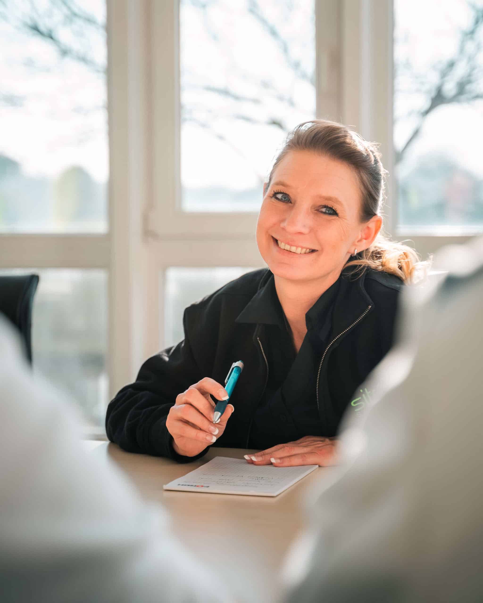 Freundliche Mitarbeiterin von Sitron am Besprechungstisch mit Schreibblock.
